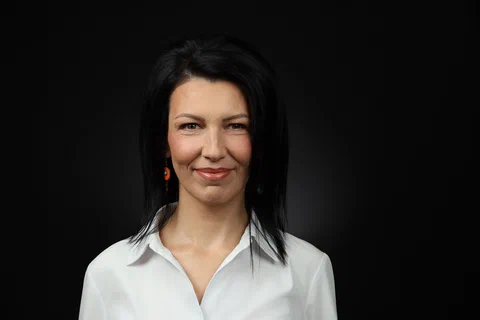 Жена с тъмна коса и естествен грим се усмихва пред тъмен фон